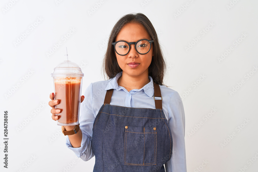 Chinese woman wearing glasses apron drinking smoothie over isolated white background with a confident expression on smart face thinking serious