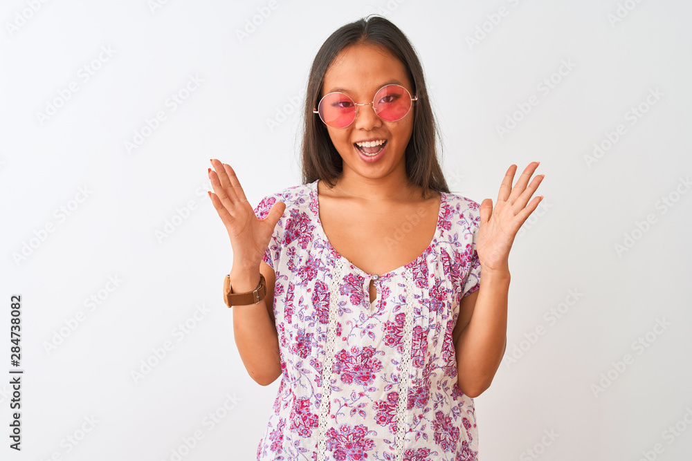 Young chinese woman wearing floral t-shirt and pink glasses over isolated white background celebrating crazy and amazed for success with arms raised and open eyes screaming excited. Winner concept Young chinese woman wearing floral t-shirt and pink glasses over isolated white background celebrating crazy and amazed for success with arms raised and open eyes screaming excited. Winner concept