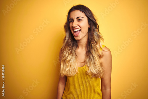 Young beautiful woman wearing t-shirt over yellow isolated background angry and mad screaming frustrated and furious, shouting with anger. Rage and aggressive concept.