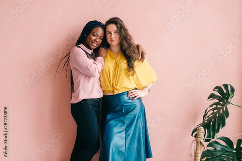 Stylish female interracial couple gugging on pink background.