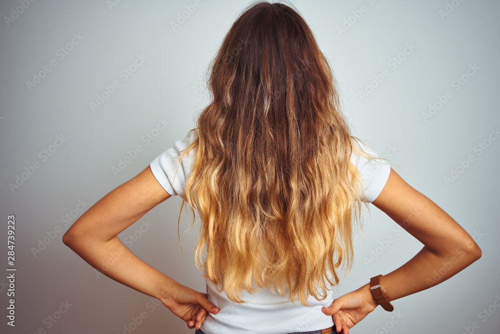 Young beautiful woman wearing casual white t-shirt over isolated background standing backwards looking away with arms on body Young beautiful woman wearing casual white t-shirt over isolated background standing backwards looking away with arms on body