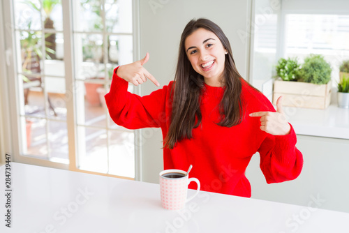 Beautiful young woman drinking a cup of black coffee looking confident with smile on face, pointing oneself with fingers proud and happy.