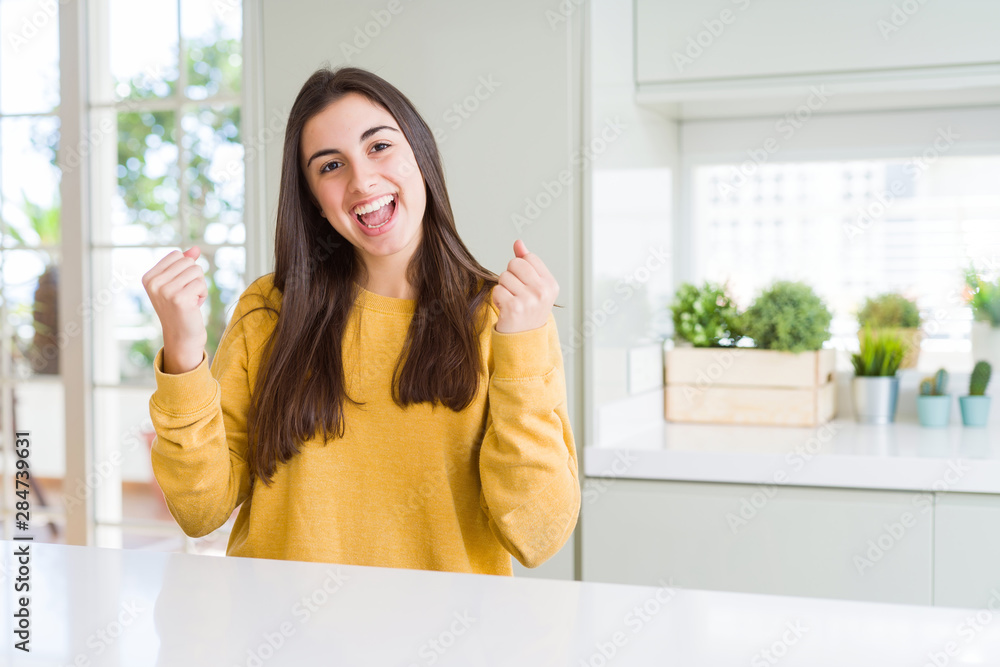 Beautiful young woman wearing yellow sweater celebrating surprised and amazed for success with arms raised and open eyes. Winner concept. Beautiful young woman wearing yellow sweater celebrating surprised and amazed for success with arms raised and open eyes. Winner concept.