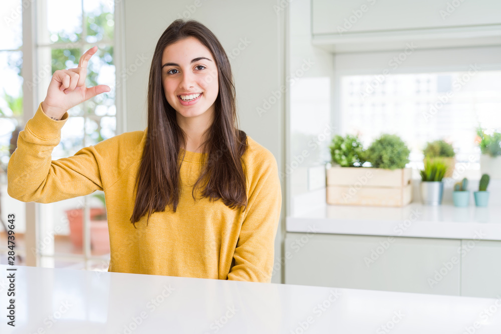 Beautiful young woman wearing yellow sweater smiling and confident gesturing with hand doing size sign with fingers while looking and the camera. Measure concept. Beautiful young woman wearing yellow sweater smiling and confident gesturing with hand doing size sign with fingers while looking and the camera. Measure concept.