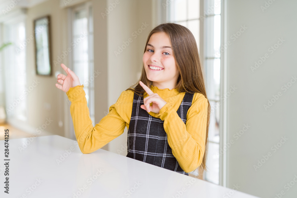 Beautiful young girl kid sitting on the table smiling and looking at the camera pointing with two hands and fingers to the side. Beautiful young girl kid sitting on the table smiling and looking at the camera pointing with two hands and fingers to the side.