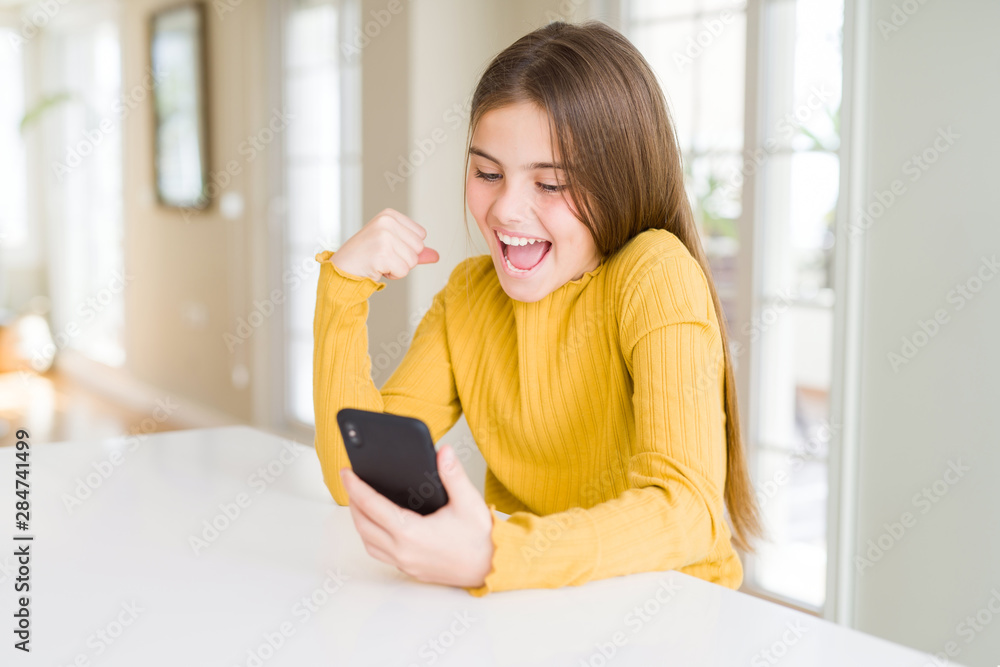 Beautiful young girl kid sending a message using smartphone screaming proud and celebrating victory and success very excited, cheering emotion Beautiful young girl kid sending a message using smartphone screaming proud and celebrating victory and success very excited, cheering emotion