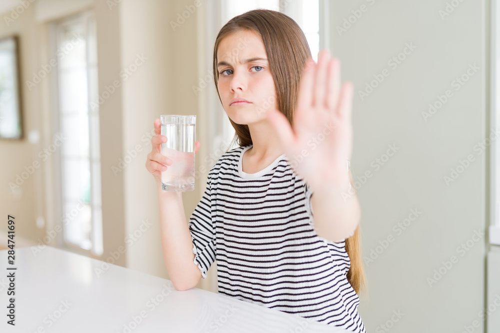 Beautiful young girl kid drinking a fresh glass of water with open hand doing stop sign with serious and confident expression, defense gesture Beautiful young girl kid drinking a fresh glass of water with open hand doing stop sign with serious and confident expression, defense gesture