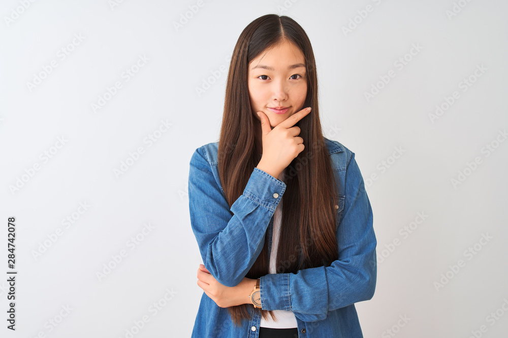 Young chinese woman wearing denim shirt standing over isolated white background looking confident at the camera with smile with crossed arms and hand raised on chin. Thinking positive. Young chinese woman wearing denim shirt standing over isolated white background looking confident at the camera with smile with crossed arms and hand raised on chin. Thinking positive.