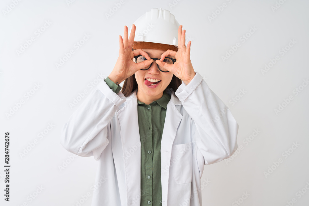 Young chinese engineer woman wearing coat helmet glasses over isolated white background doing ok gesture like binoculars sticking tongue out, eyes looking through fingers. Crazy expression. Young chinese engineer woman wearing coat helmet glasses over isolated white background doing ok gesture like binoculars sticking tongue out, eyes looking through fingers. Crazy expression.