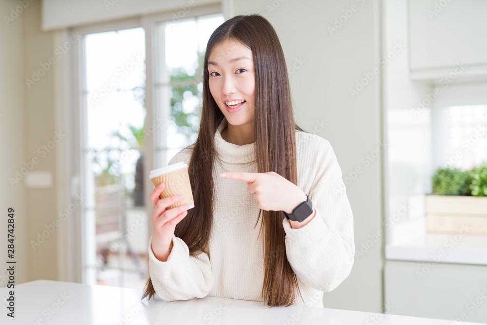 Beautiful Asian woman drinking a coffee in a take away paper cup very happy pointing with hand and finger Beautiful Asian woman drinking a coffee in a take away paper cup very happy pointing with hand and finger
