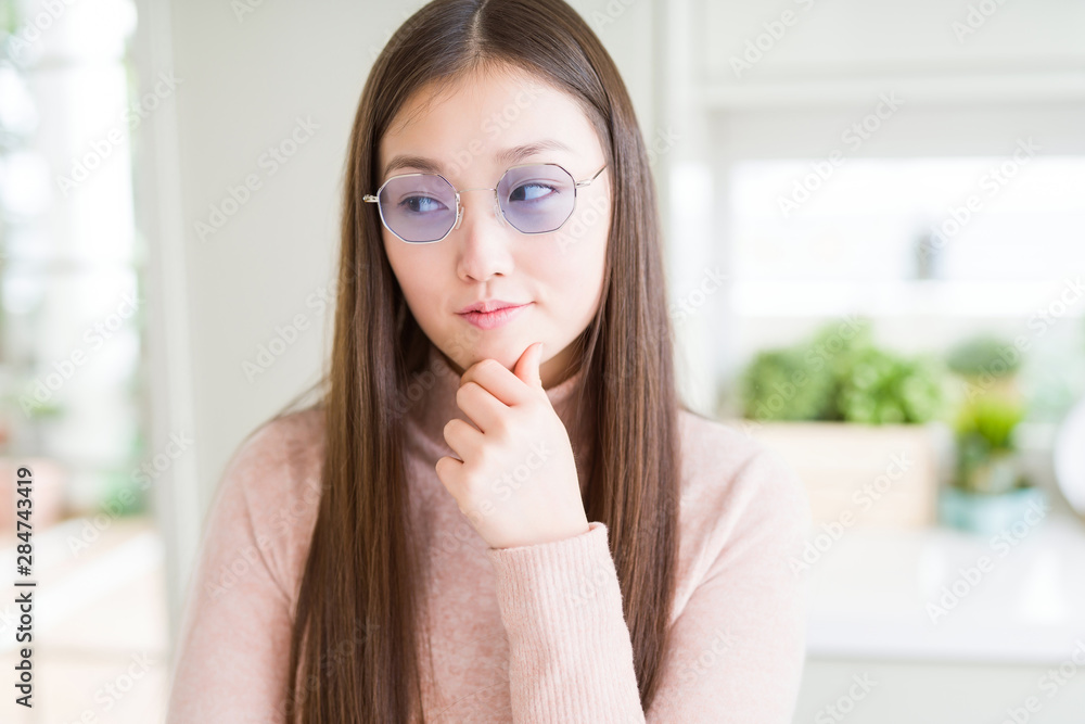 Beautiful Asian woman wearing glasses with hand on chin thinking about question, pensive expression. Smiling with thoughtful face. Doubt concept. Beautiful Asian woman wearing glasses with hand on chin thinking about question, pensive expression. Smiling with thoughtful face. Doubt concept.