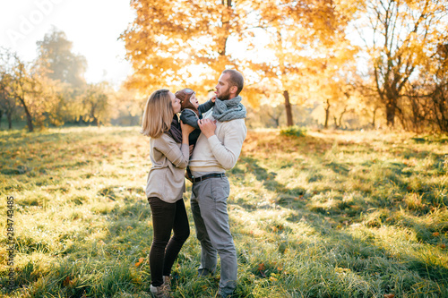 Happy family couple hugs their lovely baby in sunny autumn park.