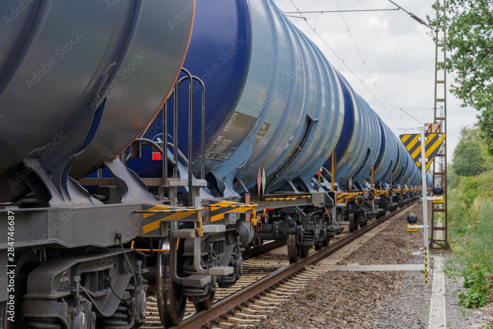 Side view of freight train with petroleum tank cars on railroad track in countryside in Europe. 