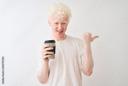 Young albino blond man drinking coffee standing over isolated white background pointing and showing with thumb up to the side with happy face smiling