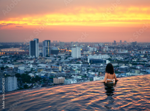 Photography Young woman relax in swimming pool on roof top during amazing sunset and enjoy c