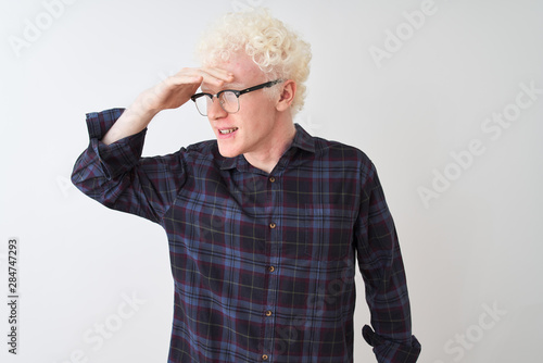 Young albino blond man wearing casual shirt and glasses over isolated white background very happy and smiling looking far away with hand over head. Searching concept.