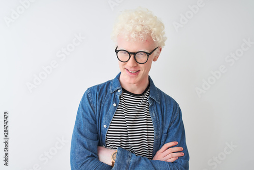 Young albino blond man wearing denim shirt and glasses over isolated white background happy face smiling with crossed arms looking at the camera. Positive person.