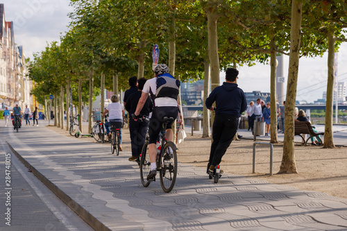 People ride E-scooters, trendy urban transportation with Eco friendly sharing mobility concept, and bicycle on bicycle lane at promenade riverside of Rhine River in Düsseldorf, Germany.