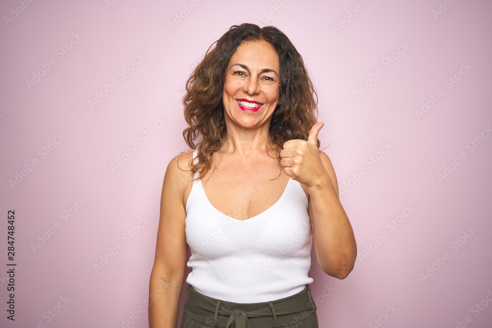 Middle age senior woman standing over pink isolated background doing happy thumbs up gesture with hand. Approving expression looking at the camera with showing success. Middle age senior woman standing over pink isolated background doing happy thumbs up gesture with hand. Approving expression looking at the camera with showing success.