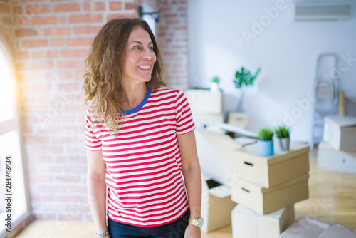 Fototapeta Naklejka Na Ścianę i Meble -  Middle age senior woman moving to a new house packing cardboard boxes looking away to side with smile on face, natural expression. Laughing confident.