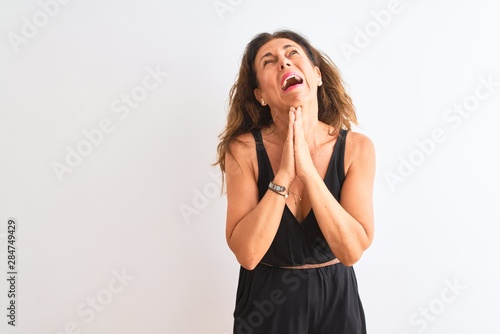 Middle age woman wearing black casual dress standing over isolated white background begging and praying with hands together with hope expression on face very emotional and worried. 