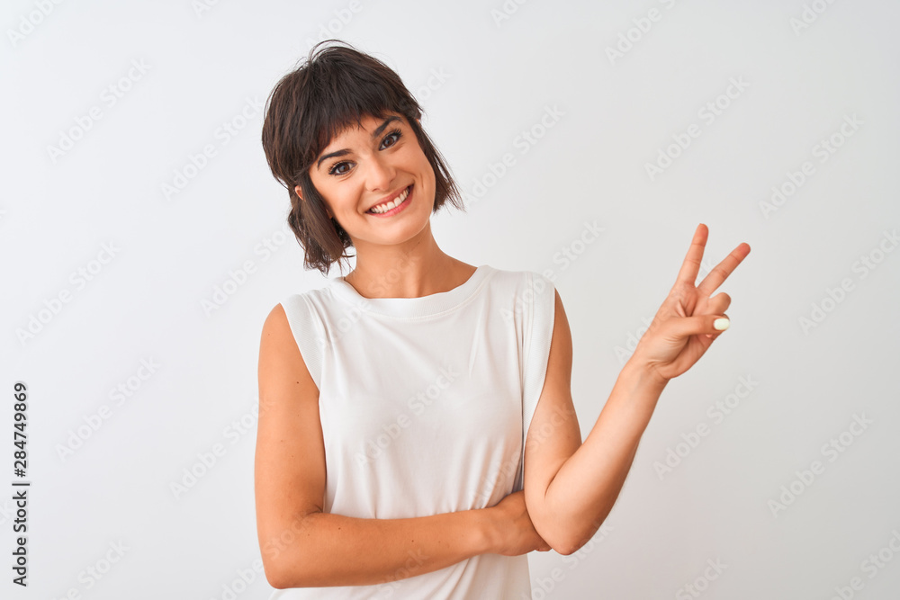 Young beautiful woman wearing casual t-shirt standing over isolated white background smiling with happy face winking at the camera doing victory sign. Number two. Young beautiful woman wearing casual t-shirt standing over isolated white background smiling with happy face winking at the camera doing victory sign. Number two.