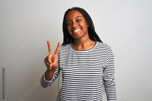 Young african american woman wearing striped t-shirt standing over isolated white background smiling looking to the camera showing fingers doing victory sign. Number two.