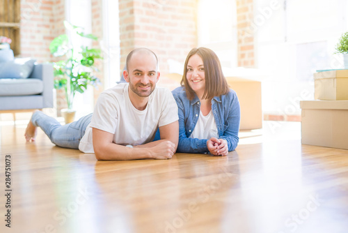 Young couple in love lying on the floor of new house arround cardboard boxes, smiling very happy for moving to a new apartment