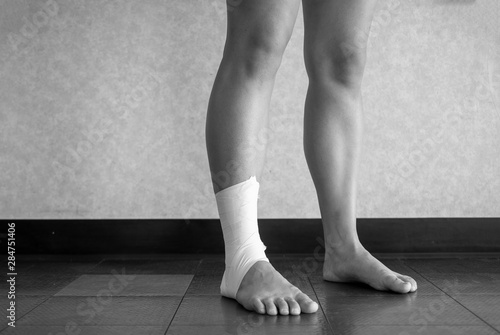 Black and white version of Athlete standing with an ankle tape job on their injured ankle 