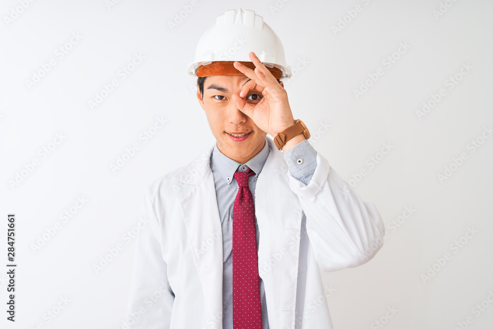 Chinese architect man wearing coat and helmet standing over isolated white background doing ok gesture with hand smiling, eye looking through fingers with happy face. Chinese architect man wearing coat and helmet standing over isolated white background doing ok gesture with hand smiling, eye looking through fingers with happy face.