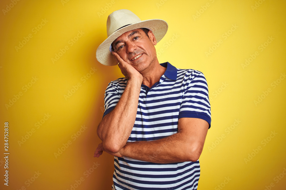 Handsome middle age man wearing striped polo and hat over isolated yellow background thinking looking tired and bored with depression problems with crossed arms.