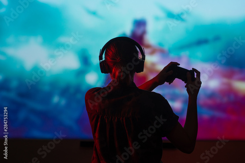 A gamer or a streamer girl at home in a dark room with a gamepad playing with friends on the networks in video games. A young man sits in front of a monitor