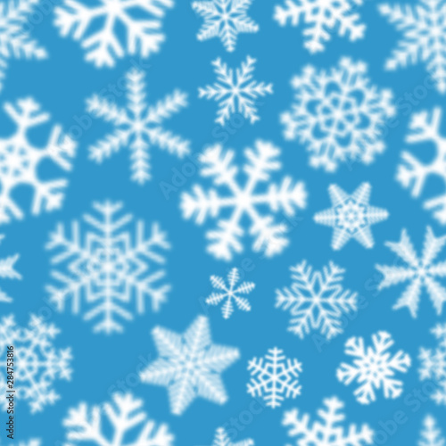 Christmas seamless pattern of white defocused snowflakes on light blue background