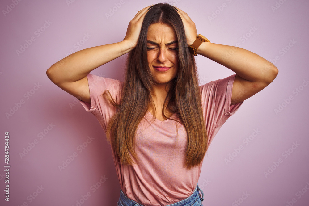 Young beautiful woman wearing t-shirt standing over isolated pink background suffering from headache desperate and stressed because pain and migraine. Hands on head. Young beautiful woman wearing t-shirt standing over isolated pink background suffering from headache desperate and stressed because pain and migraine. Hands on head.