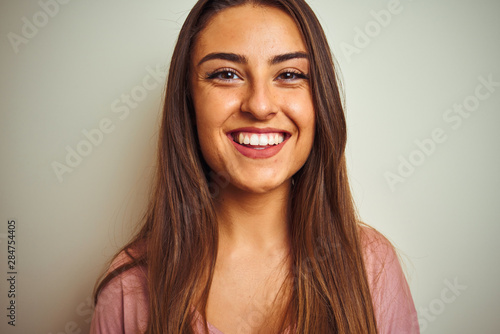 Young beautiful woman wearing pink t-shirt standing over isolated white background with a happy face standing and smiling with a confident smile showing teeth