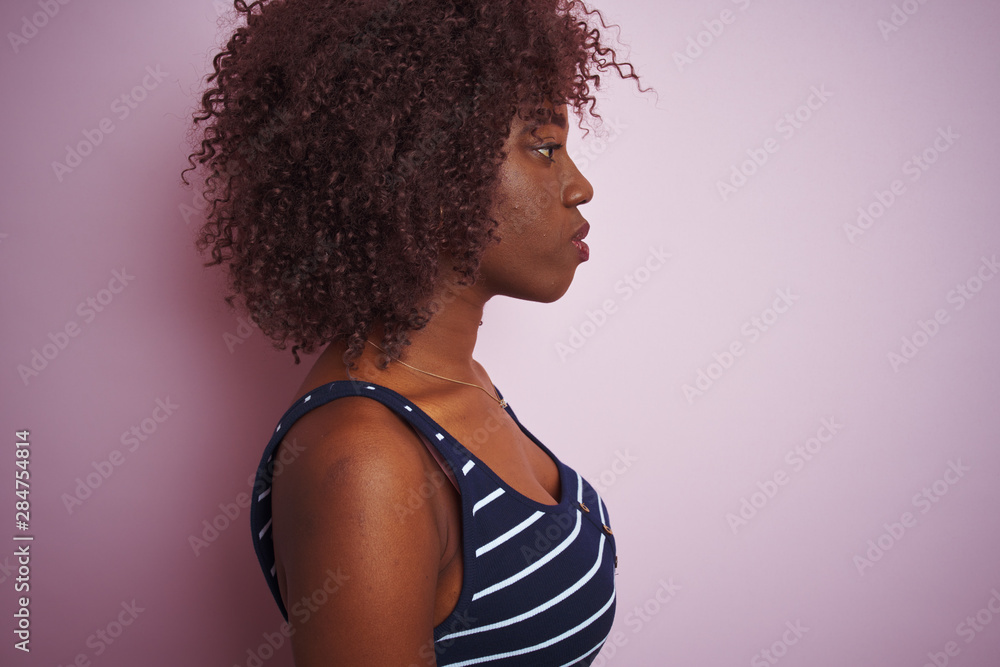 Young african afro woman wearing striped t-shirt standing over isolated pink background looking to side, relax profile pose with natural face with confident smile. Young african afro woman wearing striped t-shirt standing over isolated pink background looking to side, relax profile pose with natural face with confident smile.