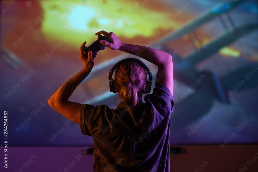 A girl gamer plays games with a gamepad, joystick on a huge screen, with creative light in a dark room. gameman A girl gamer plays games with a gamepad, joystick on a huge screen, with creative light in a dark room. gameman