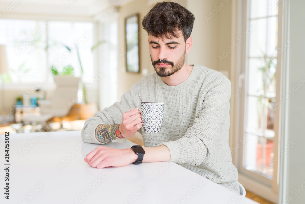 Handsome young man drinking a cup of coffee at home, enjoying warm cafe on a break