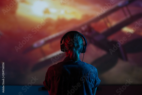 Girl gamer playing games in the headphones on a large screen, with bright light and a dark room. .bright background