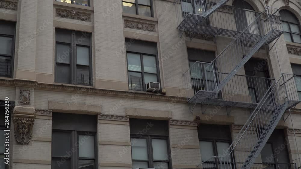 Day time establishing shot DX matching New York City style apartment building exterior. Window air conditioners and fire escape on facade structure construction view from street level Day time establishing shot DX matching New York City style apartment building exterior. Window air conditioners and fire escape on facade structure construction view from street level