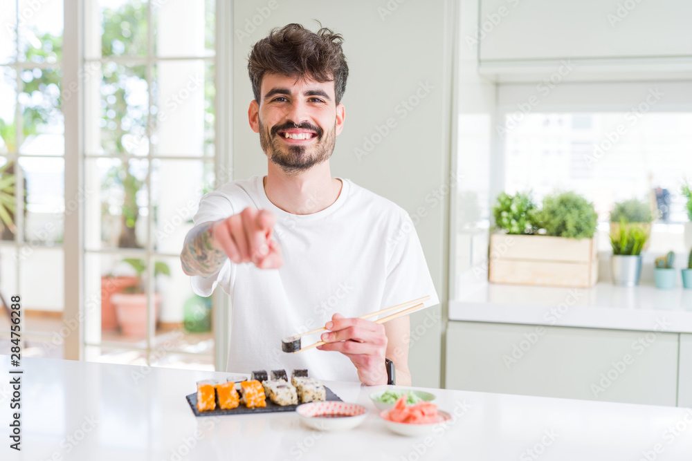 Young man eating asian sushi from home delivery pointing with finger to the camera and to you, hand sign, positive and confident gesture from the front Young man eating asian sushi from home delivery pointing with finger to the camera and to you, hand sign, positive and confident gesture from the front