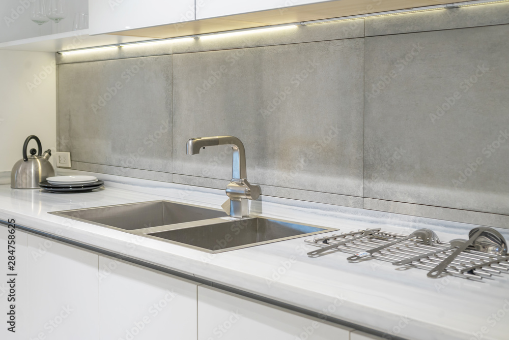 Detail of a white rectangular designer kitchen sink with chrome water tap against a tiled wall Detail of a white rectangular designer kitchen sink with chrome water tap against a tiled wall