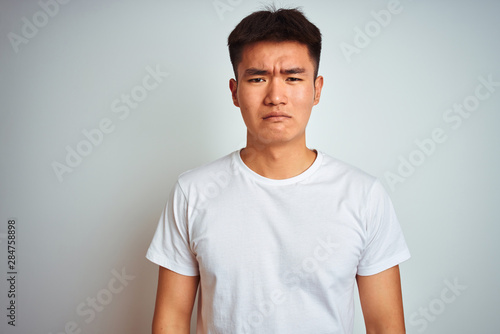 Young asian chinese man wearing t-shirt standing over isolated white background depressed and worry for distress, crying angry and afraid. Sad expression.