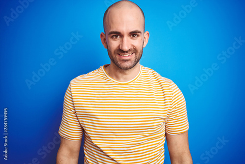 Young bald man with beard wearing casual t-shirt over blue isolated background with a happy and cool smile on face. Lucky person.