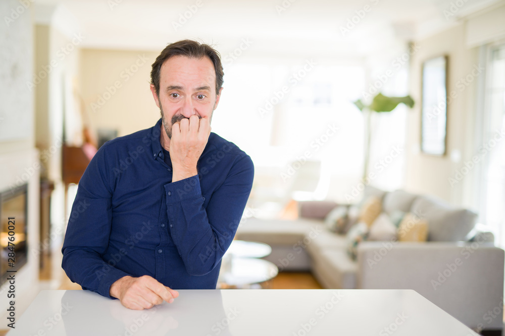 Handsome middle age man at home looking stressed and nervous with hands on mouth biting nails. Anxiety problem. Handsome middle age man at home looking stressed and nervous with hands on mouth biting nails. Anxiety problem.