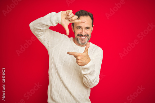 Handsome middle age senior man with grey hair over isolated red background smiling making frame with hands and fingers with happy face. Creativity and photography concept. © Krakenimages.com