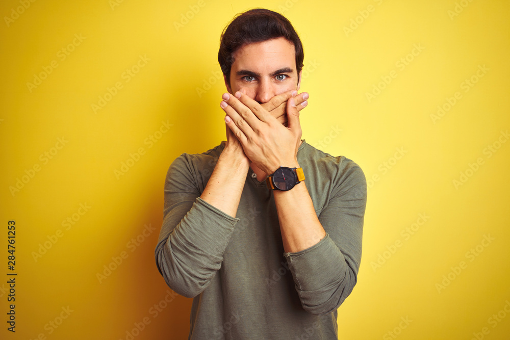 Young handsome man wearing casual t-shirt standing over isolated yellow background shocked covering mouth with hands for mistake. Secret concept. Young handsome man wearing casual t-shirt standing over isolated yellow background shocked covering mouth with hands for mistake. Secret concept.