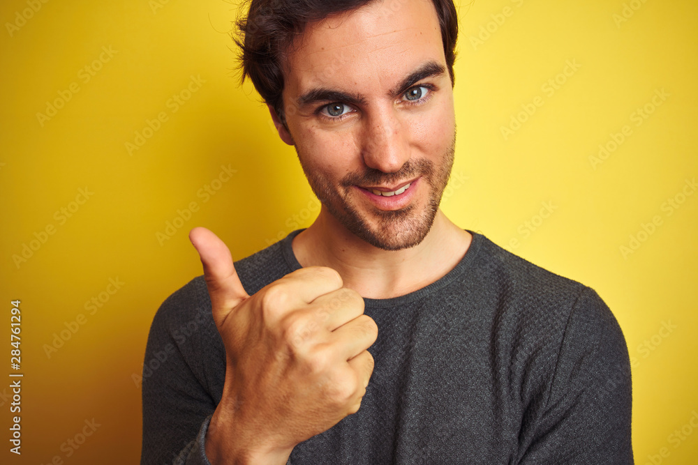 Young handsome man wearing casual sweater standing over isolated yellow background happy with big smile doing ok sign, thumb up with fingers, excellent sign Young handsome man wearing casual sweater standing over isolated yellow background happy with big smile doing ok sign, thumb up with fingers, excellent sign