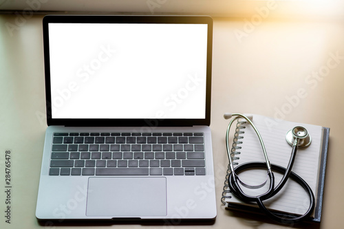 Mock up image of laptop computer with blank white screen, medical stethoscope and notebook on office desk. e health,telehealth,telemedicine or medical network concept. photo