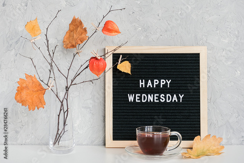 Happy Wednesday text on black letter board and bouquet of branches with yellow leaves on clothespins in vase on table Template for postcard, greeting card Concept Hello autumn Wednesday photo